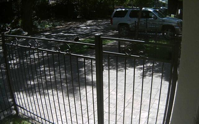 A car is parked in a driveway behind a fence
